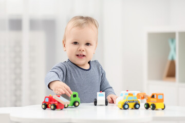 Children toys. Cute little boy playing with toy cars at white table in room