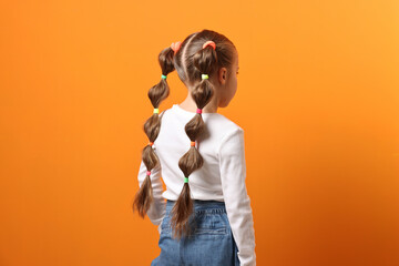 Fototapeta premium Little girl with beautiful hairstyle on orange background, back view