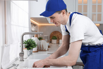 Young plumber wearing uniform repairing sink in kitchen