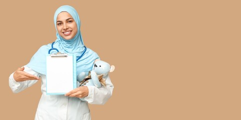 Portrait of female Muslim pediatrician holding clipboard on beige background with space for text