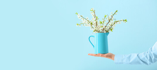 Female hand with jug of beautiful blooming branches on color background