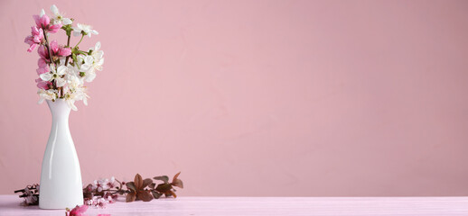 Vase with beautiful blossoming branches on table against color background