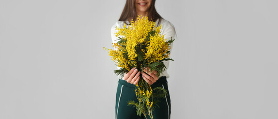 Young woman holding bouquet of beautiful mimosa flowers on light background - obrazy, fototapety, plakaty