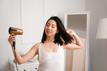 Pretty young Asian woman drying hair in bathroom