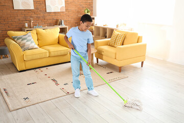 Cute African-American boy mopping floor in living room - obrazy, fototapety, plakaty