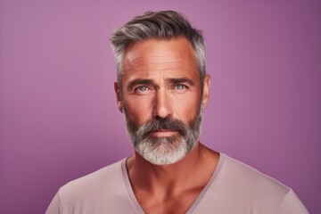 Portrait of handsome mature man with gray hair and beard. Isolated on purple background.