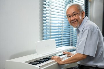 Portrait of Asian senior mature man play piano in living room at home. 