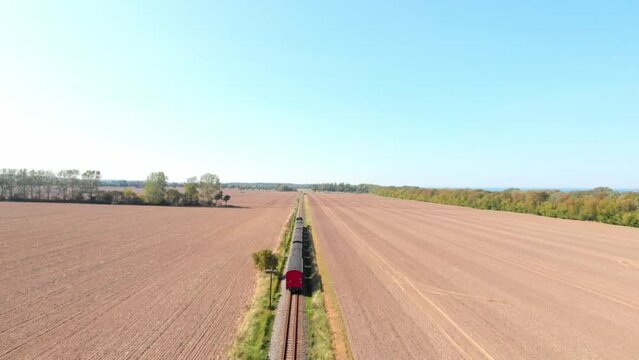 Aerial: steam narrow gauge railway in the countryside  passing by sown fields, Flying above the train