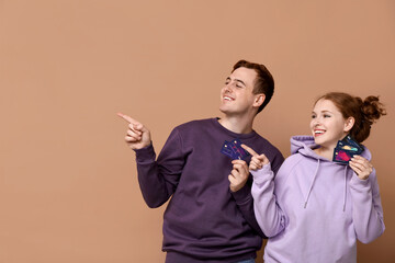 Young couple with credit cards pointing at something on brown background