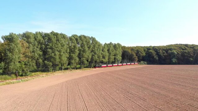 Aerial: steam narrow gauge railway in the countryside  passing by sown fields and some trees