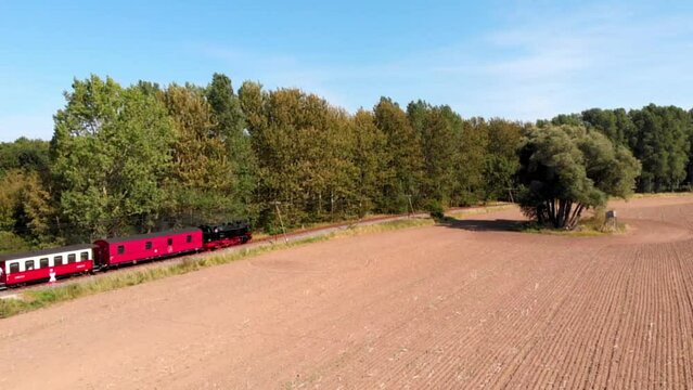 Aerial: steam narrow gauge railway in the countryside  passing by sown fields and some trees