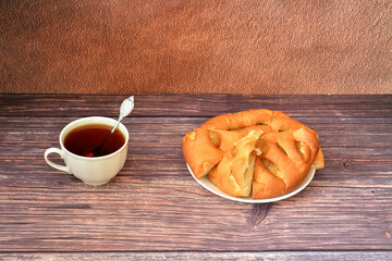 A cup of hot tea with a spoon and a plate with slices of fresh apple pie on a wooden table.