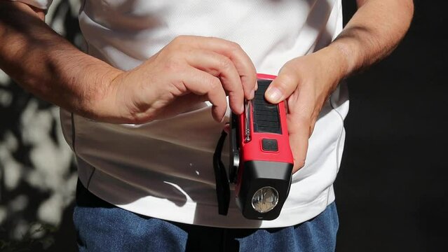 A person demonstrates how to operate a small red portable radio that is rechargeable with solar panels or manually with a crank and flashlight included