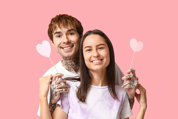 Young couple with paper hearts on pink background