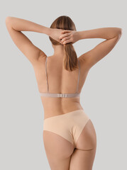 Beautiful young woman in stylish beige underwear on grey background, back view
