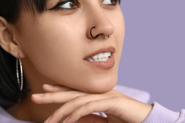Stylish young woman with nose piercing on lilac background, closeup