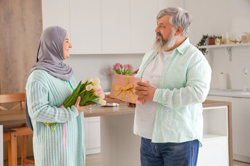 Mature Muslim man greeting his wife with gift in kitchen. Ramadan celebration