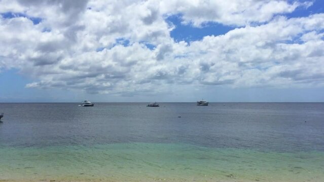 Three boats are anchored on the coastline of Siquijor Island. There are many clouds in the blue sky. The beautiful landscape of a tropical island in the Philippines.