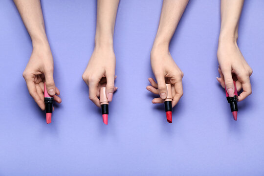 Female hands with lipsticks on purple background