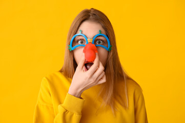 Beautiful young shocked woman in funny disguise on yellow background. April Fools Day celebration