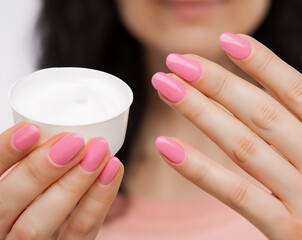 Female fingers with pink painted nails and skin cream. Hands with shiny pink gel manicure, skin care.