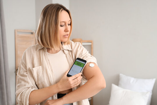 Diabetic woman with glucose sensor using mobile phone for measuring blood sugar level in bedroom
