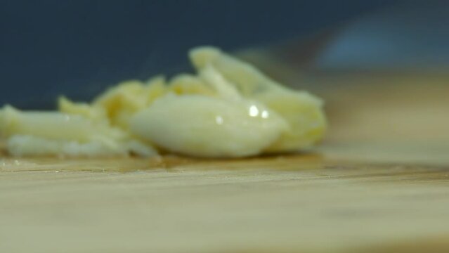 Extreme closeup: Knife chops cloves of garlic on wooden cutting board