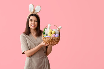 Female massage therapist in bunny ears with Easter eggs and herbal bags on pink background