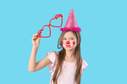 Funny girl in clown costume with party glasses on blue background. April Fool's Day celebration