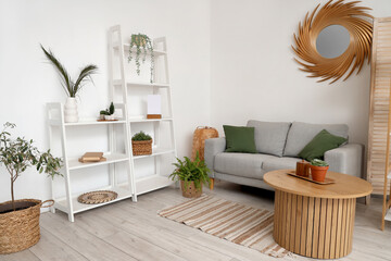 Stylish interior of light living room with shelving units, houseplants, mirror, table and sofa