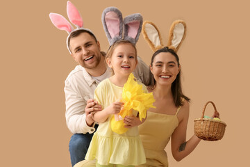 Happy family in bunny ears holding basket with Easter eggs and gift on beige background