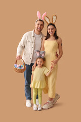 Happy family in bunny ears holding basket with Easter eggs on beige background