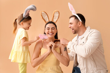 Little girl with her father in Easter bunny ears tickle mother on beige background