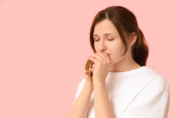 Religious young woman praying on pink background
