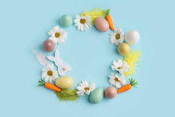 Easter wreath made of eggs, chamomiles, fabric bunny and toy carrots on blue background