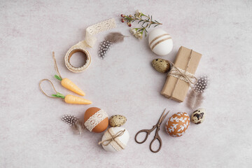 Wreath made of Easter eggs, gift box, lace, scissors and toy carrots on light background