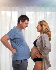 Fototapeta premium A pregnant girl and her husband measure their bellies