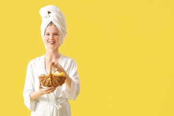 Beautiful young woman after shower holding basket with Easter eggs and essential oil on yellow...