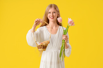Beautiful young woman holding Easter basket with spa accessories and tulip flowers on yellow background