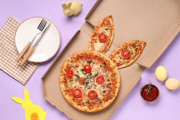Cardboard box of Easter pizza with ears, eggs and cutlery on lilac background