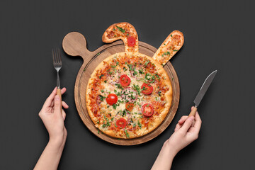 Female hands holding cutlery and Easter pizza with bunny ears on black background