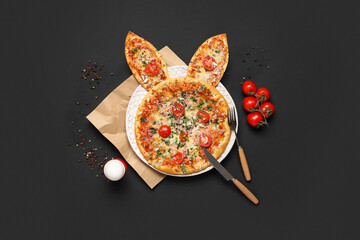 Tasty Easter pizza with bunny ears, egg, tomatoes and cutlery on black background