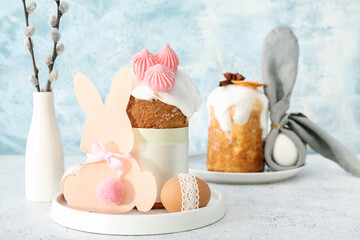 Plates with Easter cakes, eggs, and paper bunny on white table