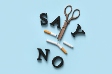 Wooden phrase SAY NO and scissors with cut cigarettes on blue background. Stop smoking concept.