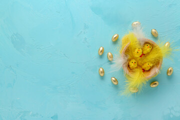 Wooden bowl with toy chick, feathers and chocolate eggs in foil on blue background. Easter concept.