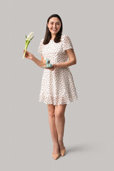Young woman with sweet Easter cake, toy bunny and beautiful flowers on grey background