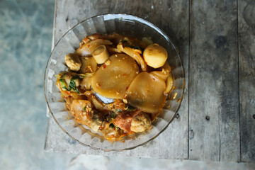 Seblak is a typical Indonesian dish with a savory and spicy taste. cooked with vegetables, sausage, eggs, chicken feet, seafood and processed beef. a bowl of seblak on a wooden table.