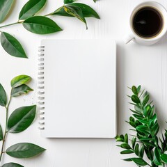 Blank white spiral notebook on table surrounded by coffee and green leaves, in flat lay photography style with minimalist aesthetic, taken from top view perspective on white background.