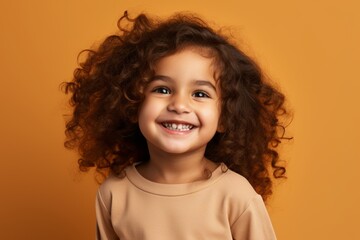 Portrait of a smiling little girl with curly hair on orange background