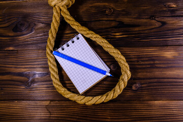 Rope with noose for the suicide, blank notepad and pen on wooden background